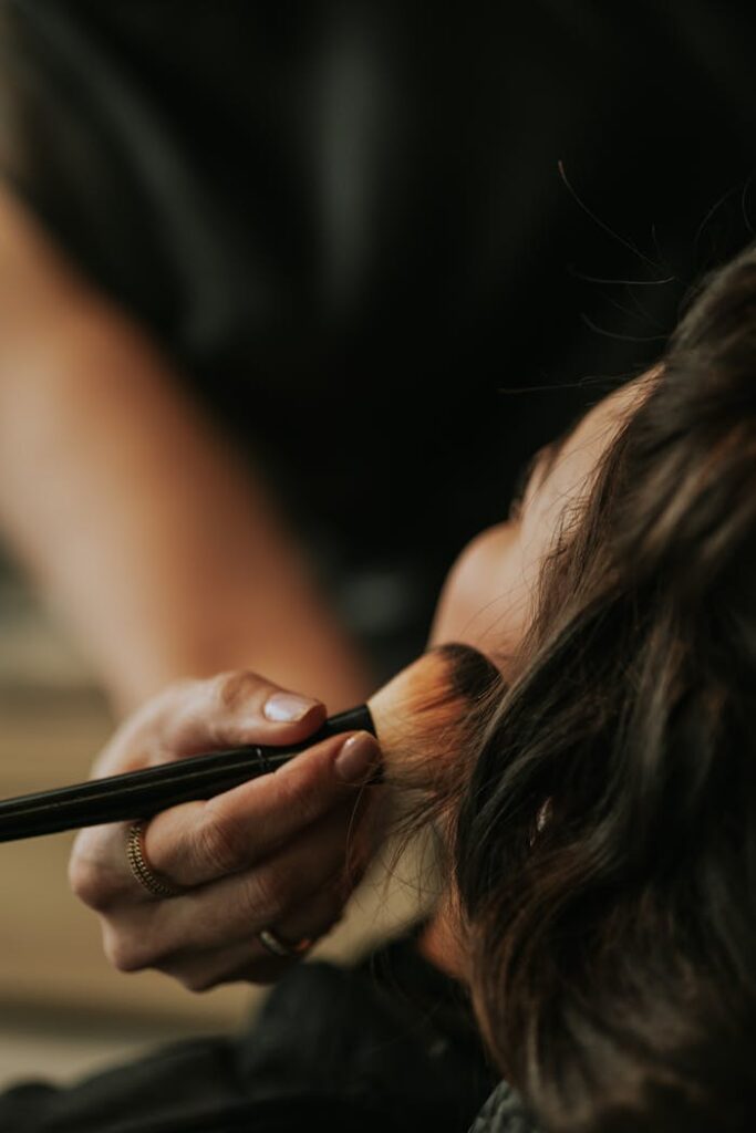 Close-up view of a professional makeup artist applying blush on a woman's face.